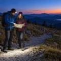 Dos senderistas con frontales y mochilas consultando un mapa en una senda al anochecer